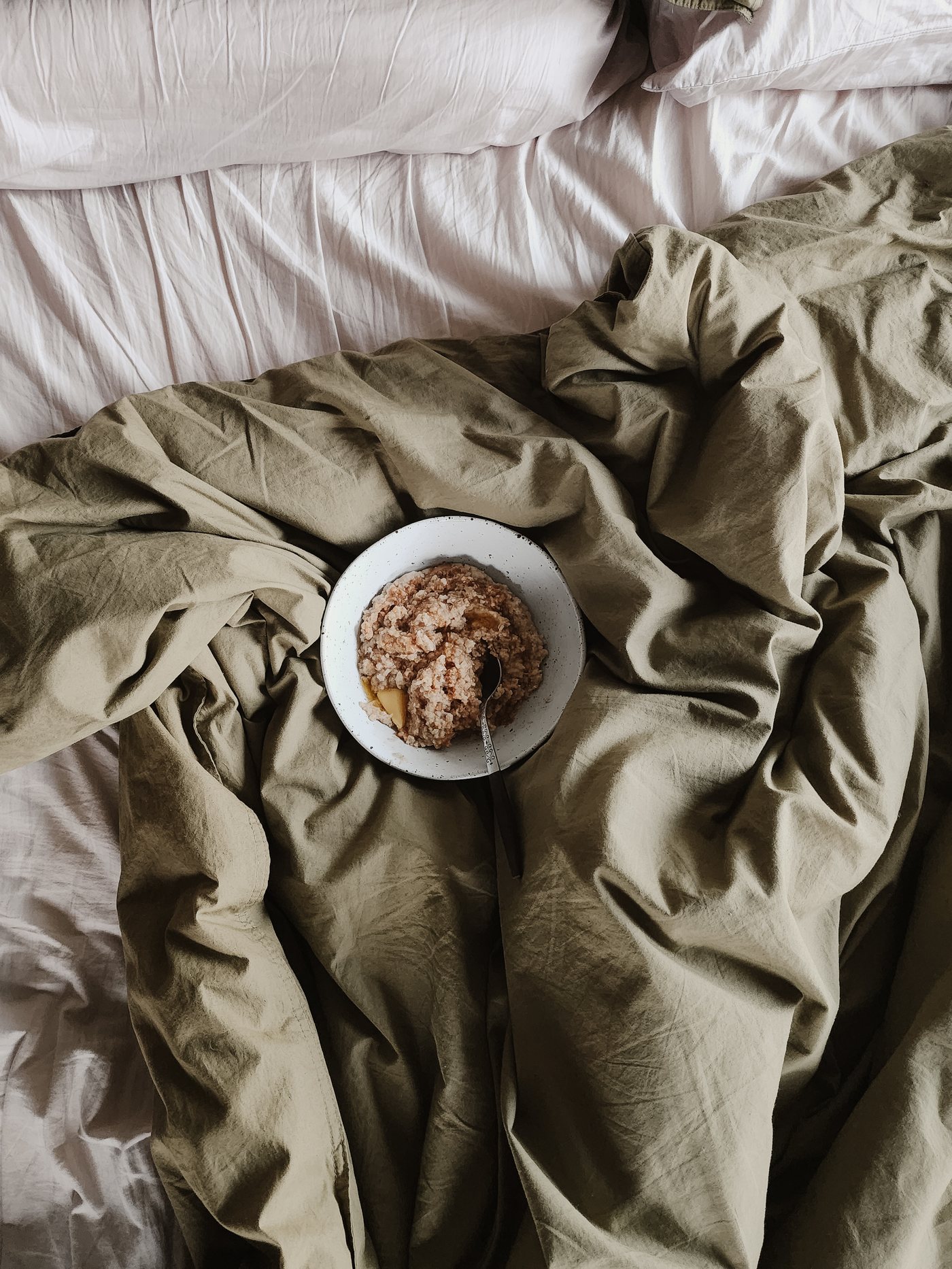 A bowl of porridge with pear, resting on a rumpled bed
