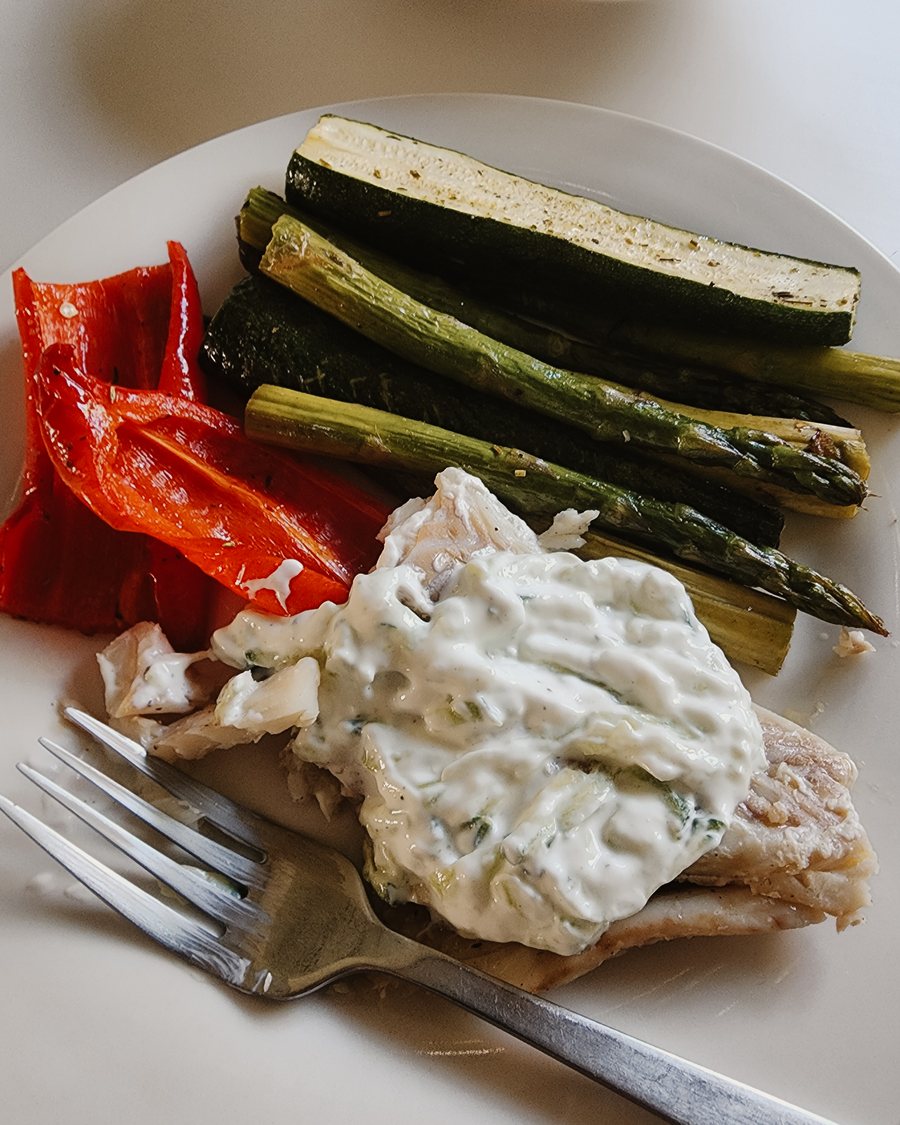 Fish with tzatziki and roasted vegetables on a white plate